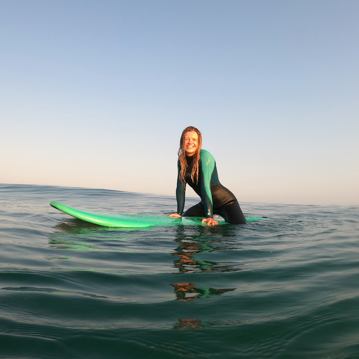 A girl out on a surf board in the ocean. She is sitting on a green board. 