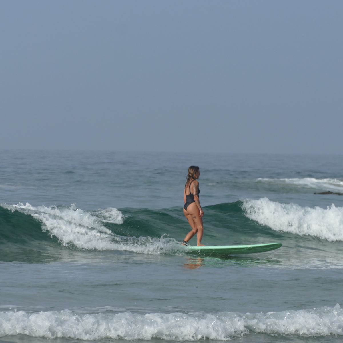 A women surfing in Morocco on a green surfboard in a swimsuit